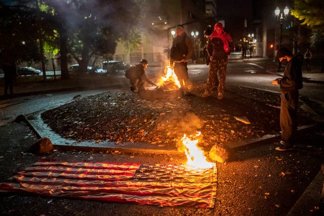 A small group of protesters watch a burning American Flag as they gather in front of the Multnomah County Justice Center early in the morning on November 4, 2020 in Portland, Oregon, as the U.S. election results poured in. 