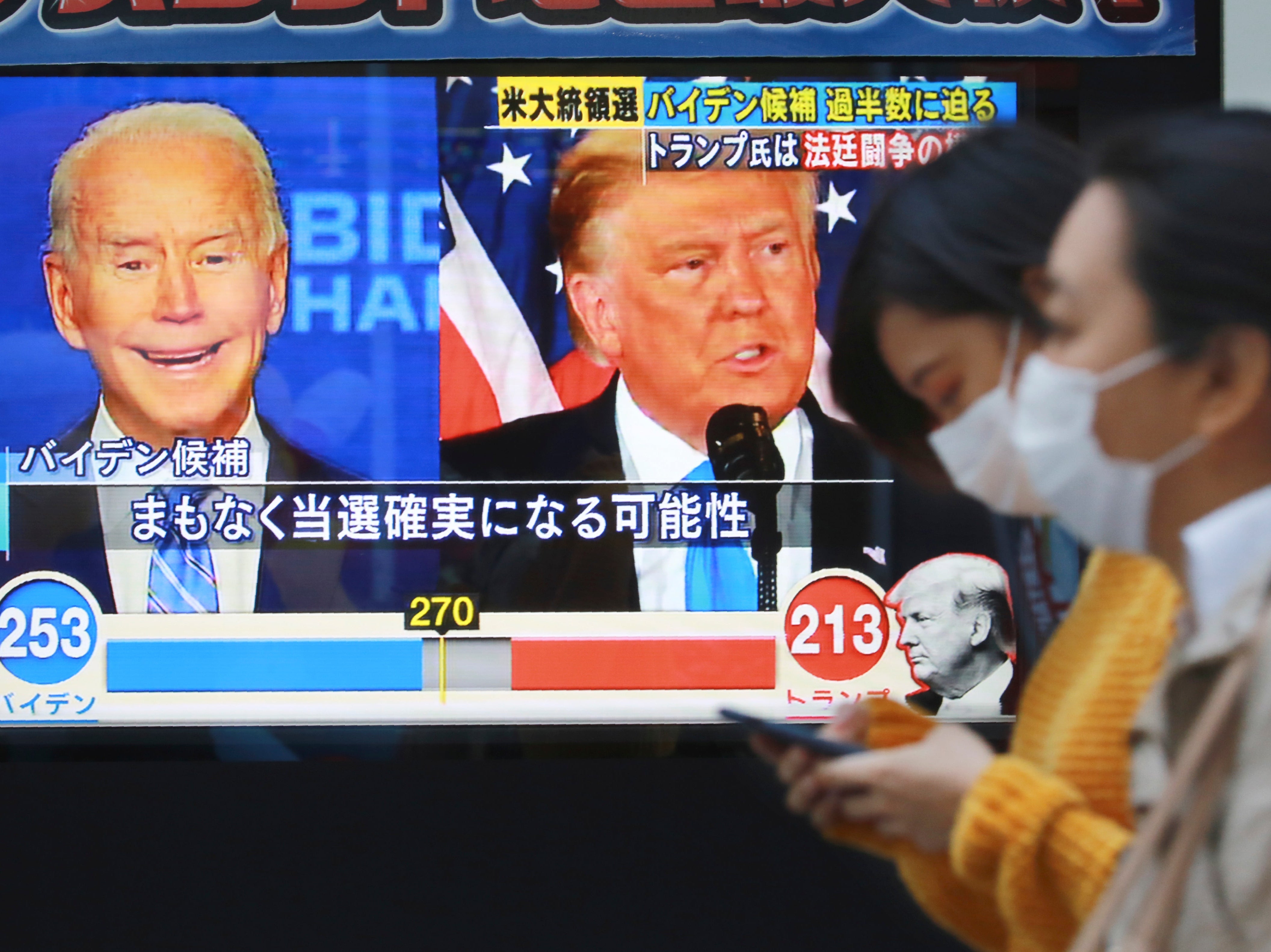City goers pass a TV screen reporting on the US election in Tokyo