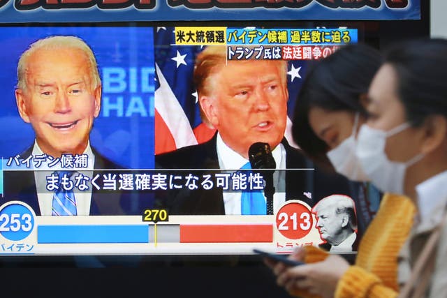 <p>City goers pass a TV screen reporting on the US election in Tokyo</p>
