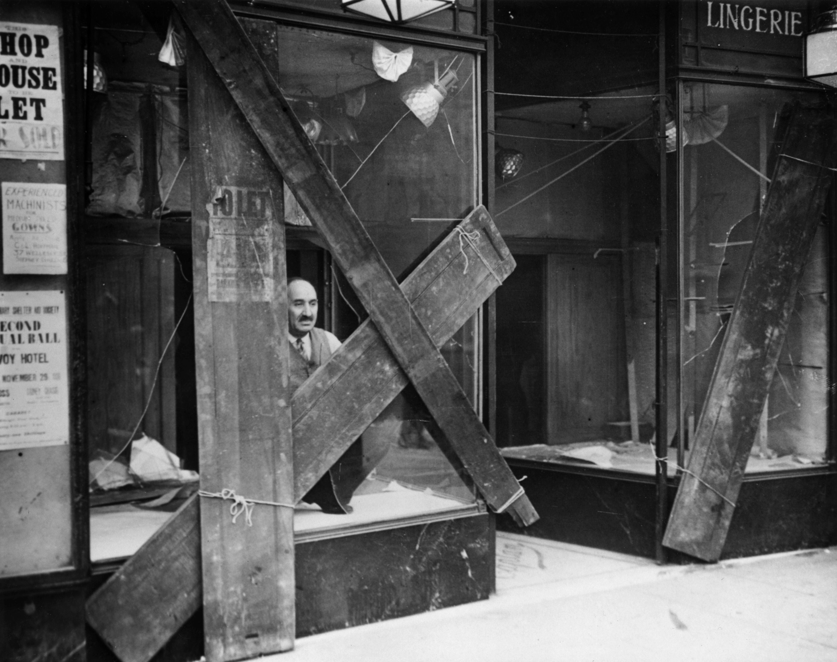 A Jewish shopkeeper peers out of his boarded up window in Mile End Road after a night of violence between fascist and communist factions in the East End of London&nbsp;