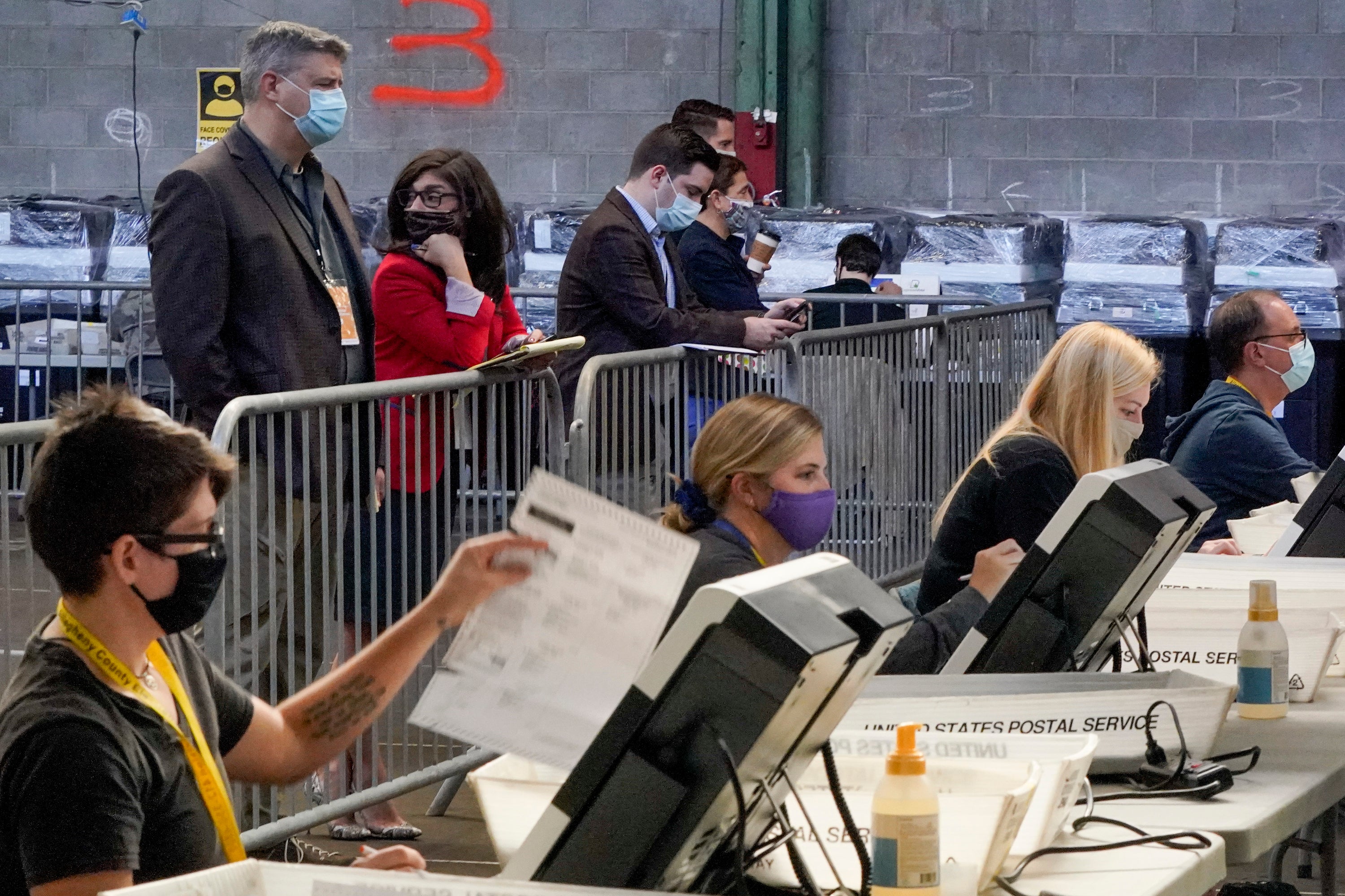 Election observers stand behind a barrier and watch as election office workers process ballots as counting continues from the general election at the Allegheny County elections returns warehouse in Pittsburgh on 6 November.