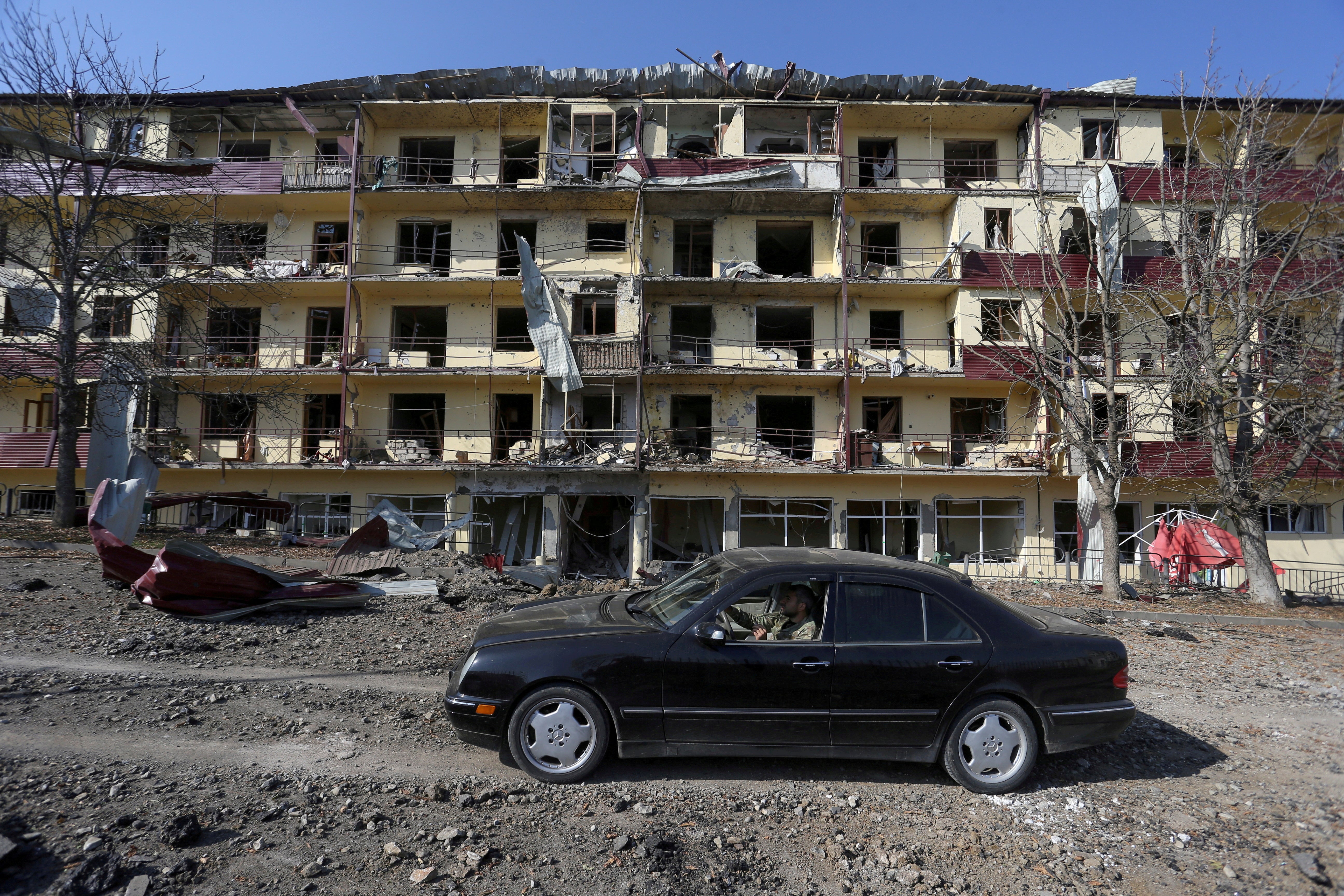 A man drives a car past a damaged building following recent shelling in the town of Shushi