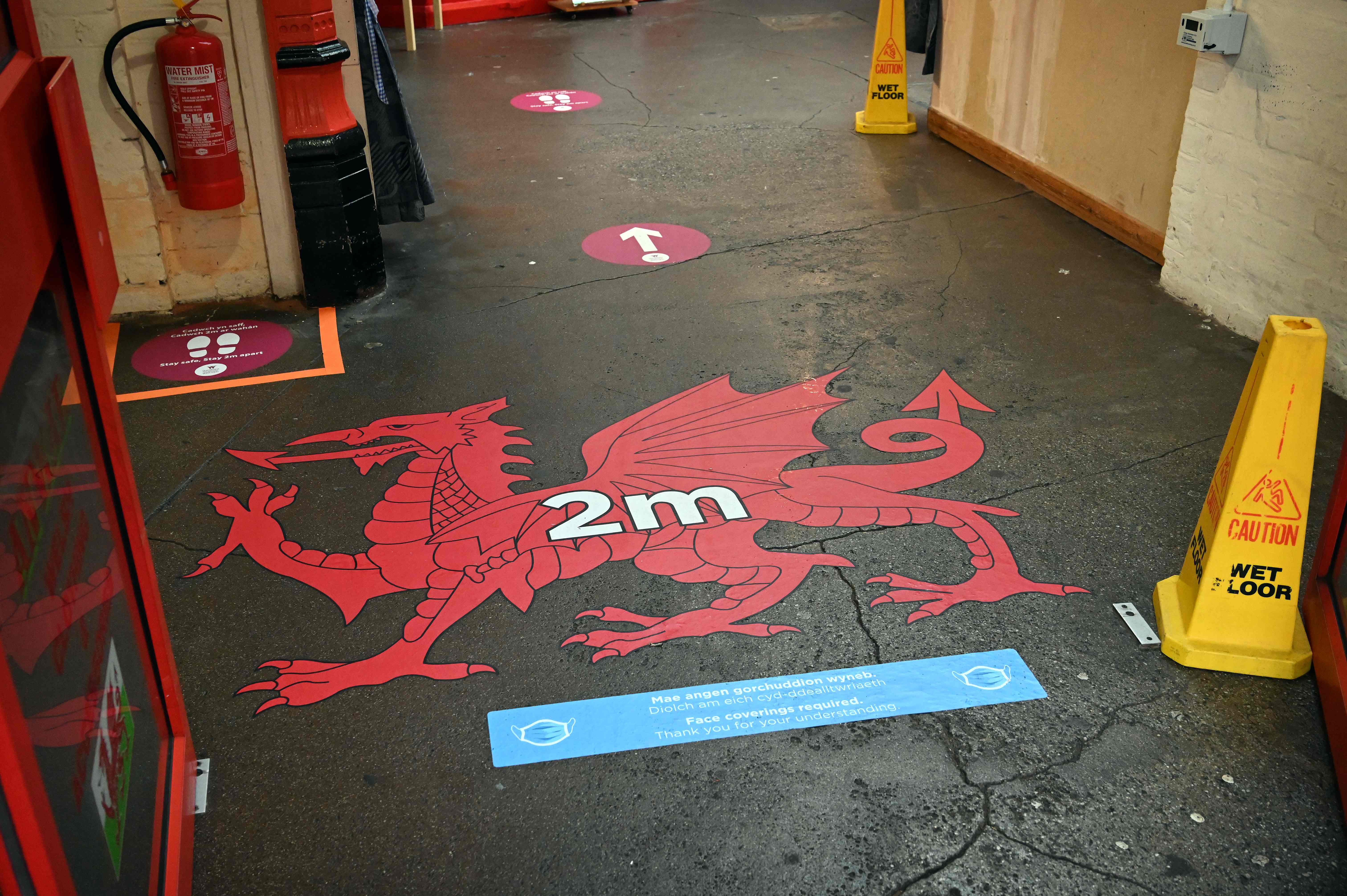 Signage encouraging social distancing as a measure to combat infections of the novel coronavirus are seen on the floor at the entrance of the market in Wrexham, North Wales