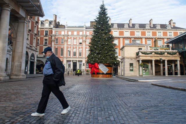 A man wearing a face mask passes the Christmas tree in Covent Garden Piazza, London