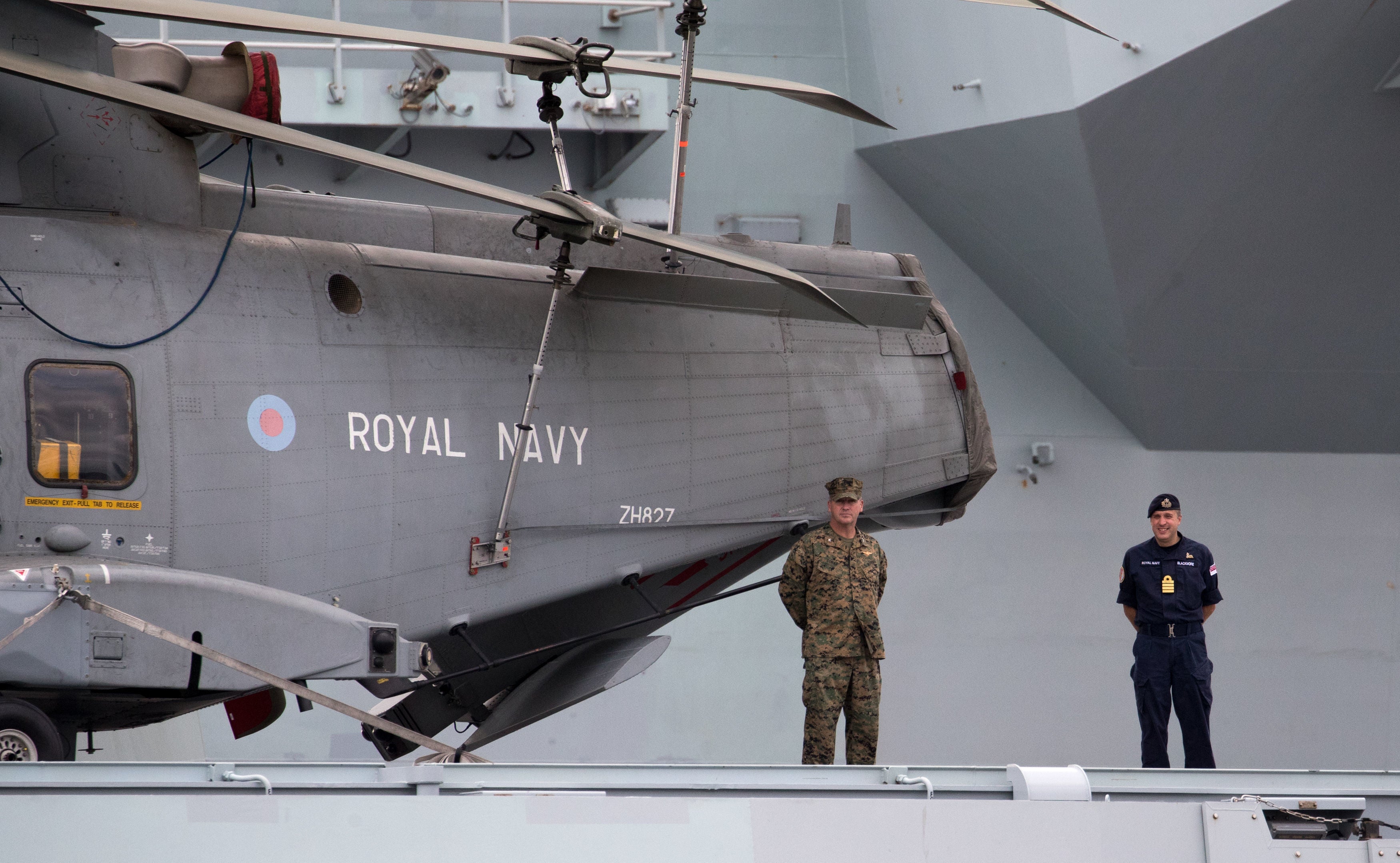 A Royal Navy officer and a member of the US Marines stand next to a Merlin helicopter on the flight deck as the Royal Navy aircraft carrier HMS Queen Elizabeth (Andrew Matthews/PA Wire)