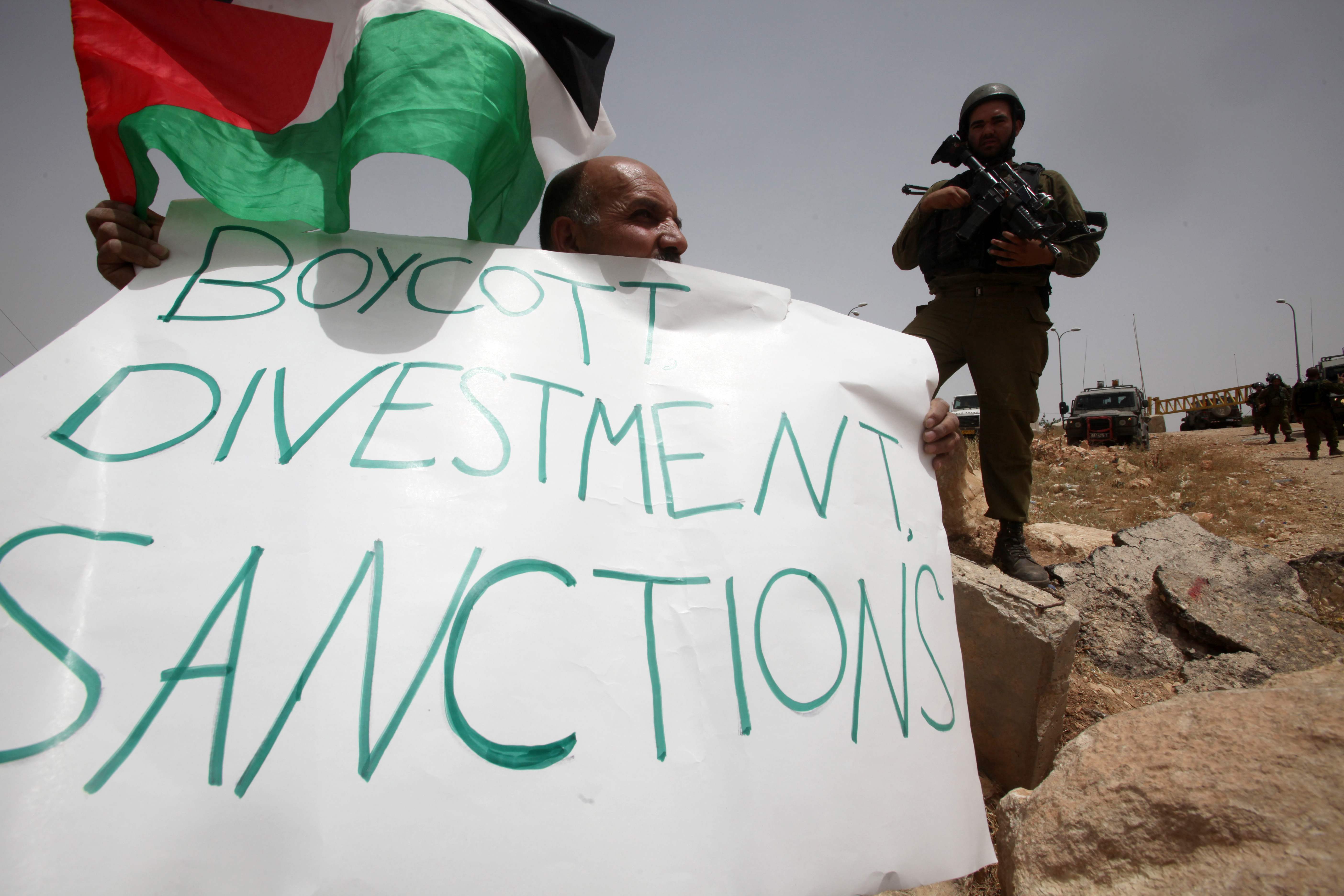 A Palestinian holds a placard that reads ‘Boycott, divestment, sanctions’