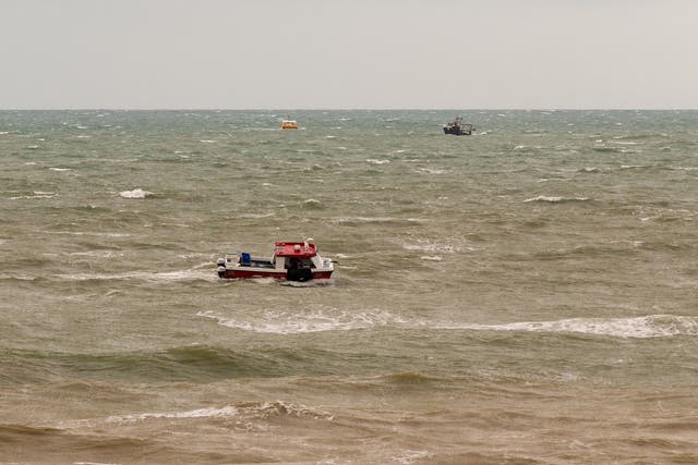 Fishing boats look for colleagues after fishing boat sinks as a search and rescue helicopter looks from above