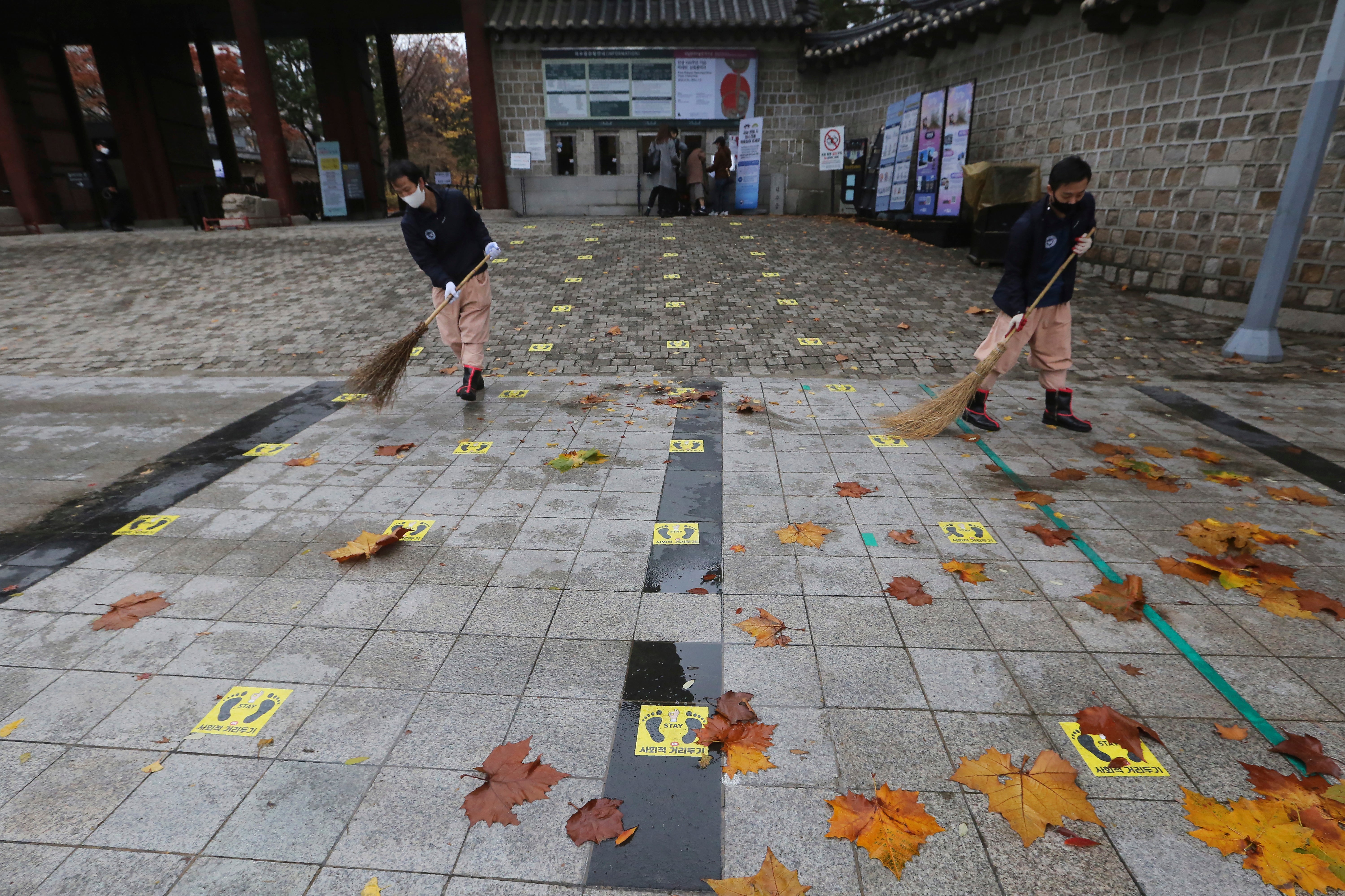 Social distancing signs are seen on the road as people clean fallen leaves in front of the Deoksu Palace in Seoul, South Korea