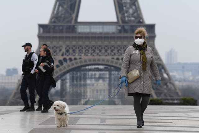 A woman wearing a protective mask walks her dog in Paris