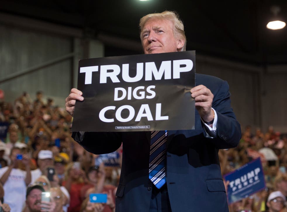 Donald Trump holds up a 'Trump Digs Coal’ sign as he arrives at a rally in West Virginia in August 2017