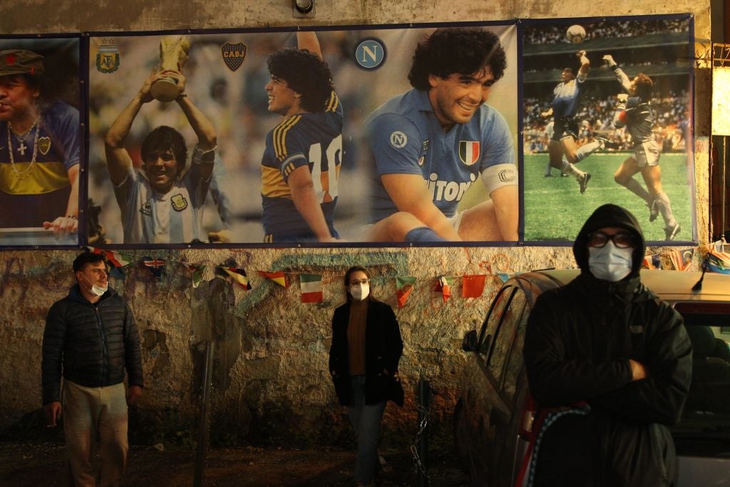 People wearing a face mask stand at the so-called "Maradona Corner" at the top of the Quartieri Spagnoli in Naples
