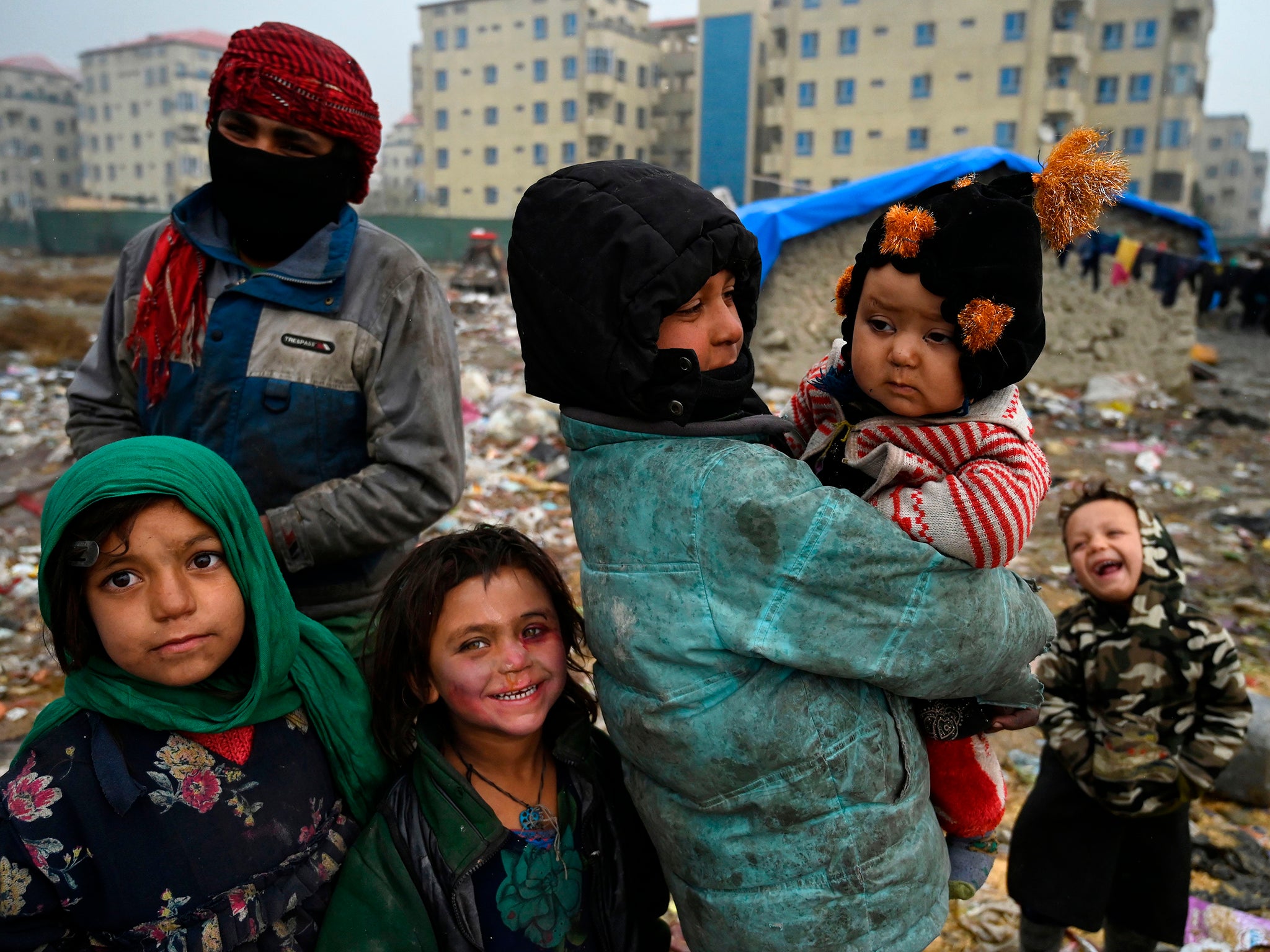 Internally displaced Afghan children stand outside their temporary mud house at a refugee camp in Kabul