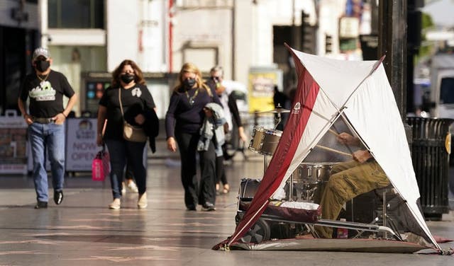 Transeúntes con mascarillas para protegerse del coronavirus pasan cerca de una tienda de campaña en la que el músico callejero Patrick La May toca la batería el martes 10 de noviembre de 2020 en el Paseo de la Fama de Hollywood, en Los Ángeles.