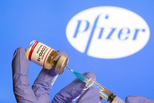 <p>Una mujer sostiene una pequeña botella etiquetada con una etiqueta adhesiva de "Vacuna contra el coronavirus COVID-19" y una jeringa médica frente al logotipo de Pfizer que se muestra el 30 de octubre de 2020.</p>