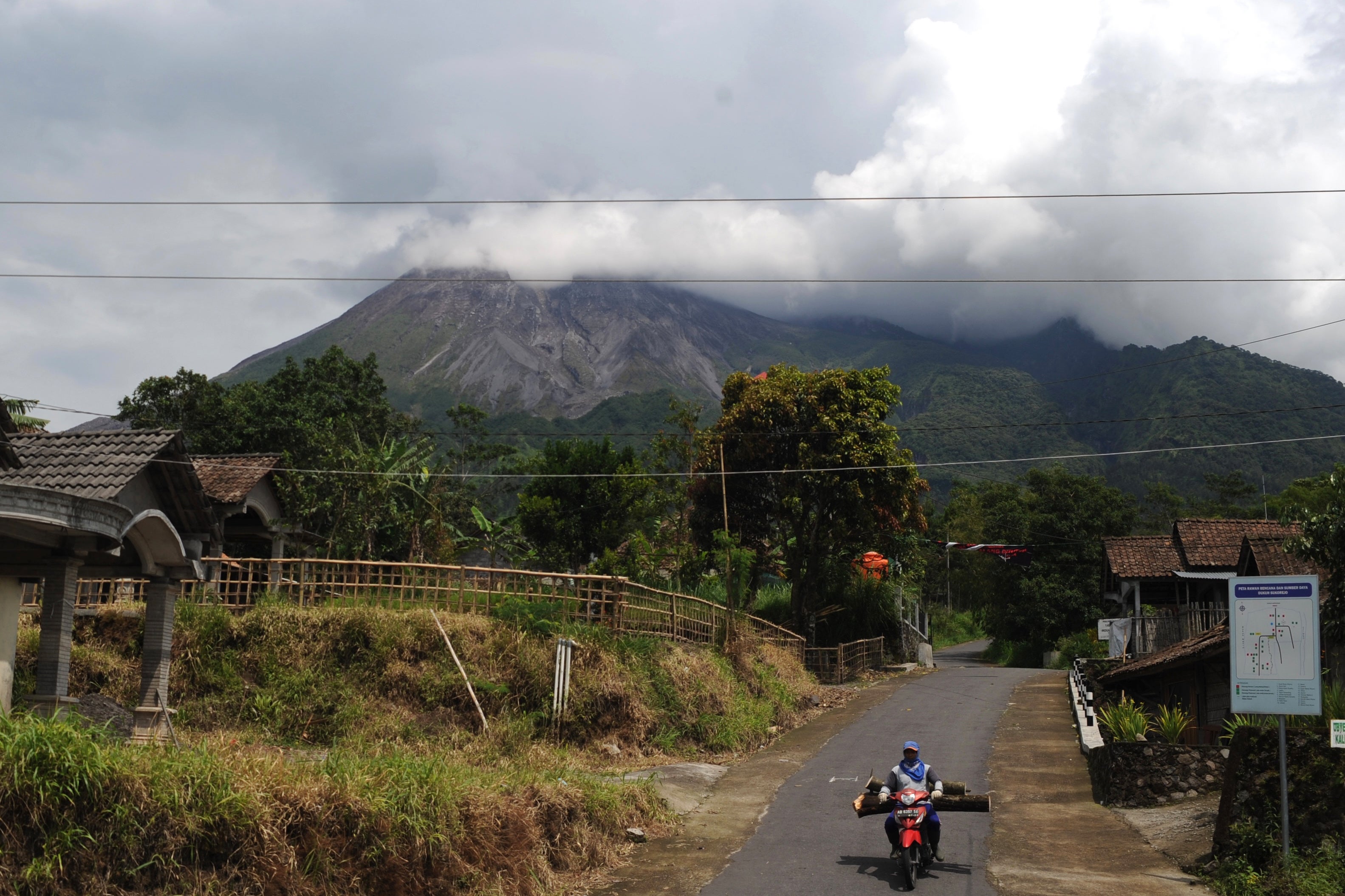 Un aldeano monta sus motocicletas a lo largo de un camino de la aldea mientras el humo se escupe desde el Monte Merapi en Yogyakarta el 27 de noviembre de 2020, después de que el Organismo Geológico de Indonesia elevara la alerta de estado del Merapi al segundo nivel más alto antes de una posible erupción. 