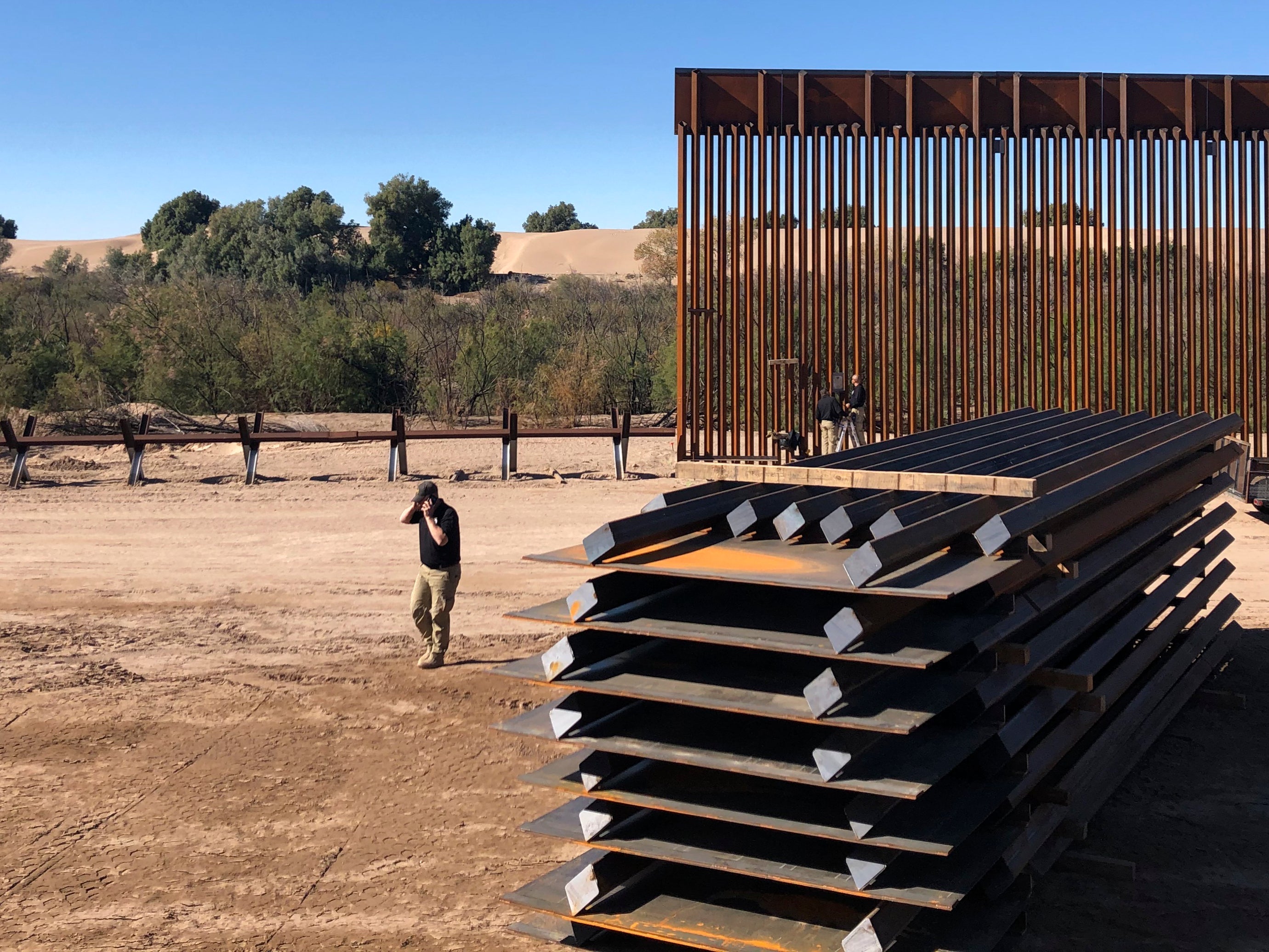 A man passes new border wall sections, right, as they replace the old fencing, left, Friday, Jan. 10, 2020, near Yuma, Arizona