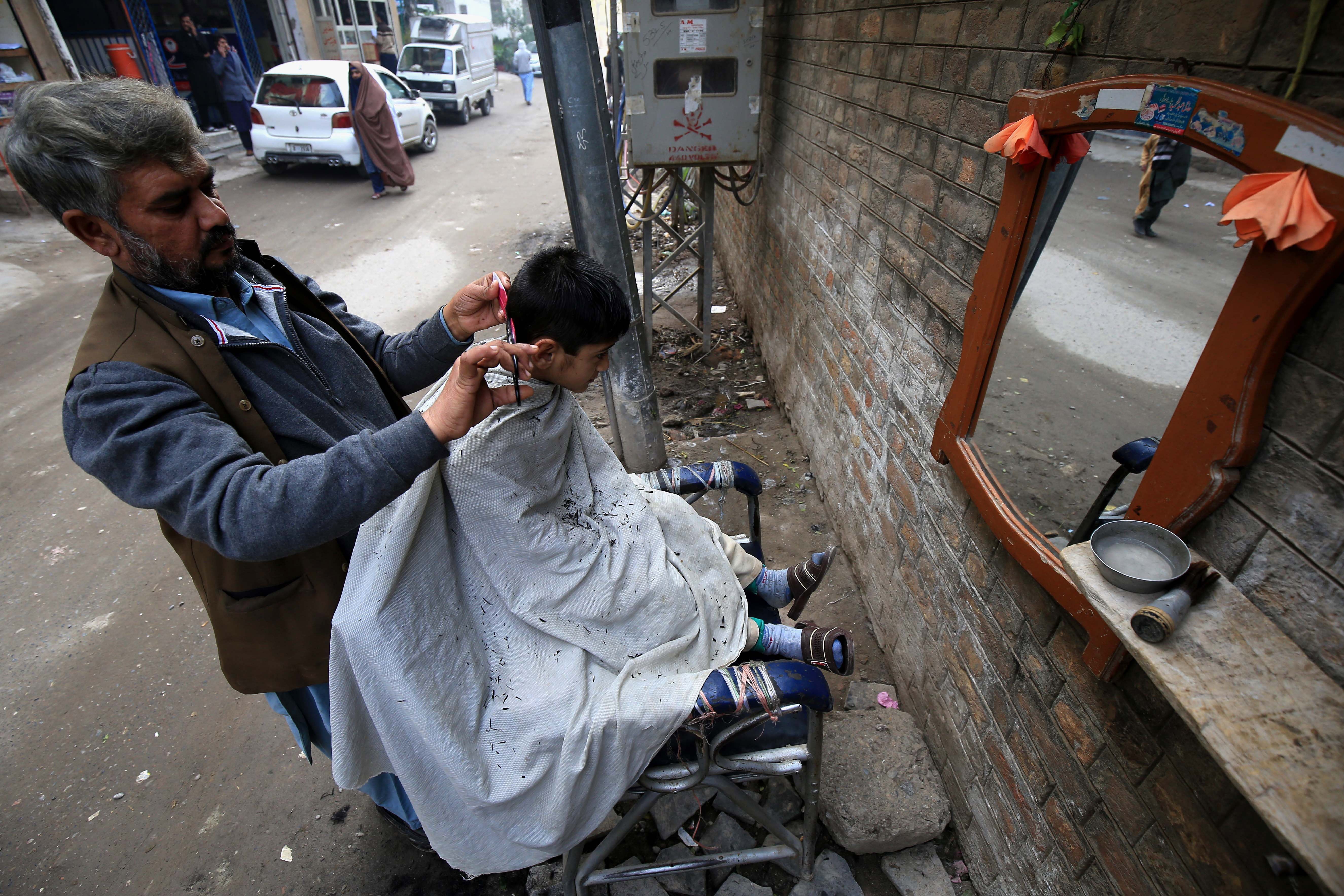 A barber gives a haircut to a customer at a roadside shop during World AIDS Day in Peshawar, Pakistan, 01 December 2020. According to doctors, cuts from razor blades that haven’t undergone proper sterilization are among some of the main causes of AIDS spread. World AIDS Day, observed annually on 01 December, is dedicated to raising awareness against the spread of AIDS and HIV infections. (EPA/ARSHAD ARBAB)