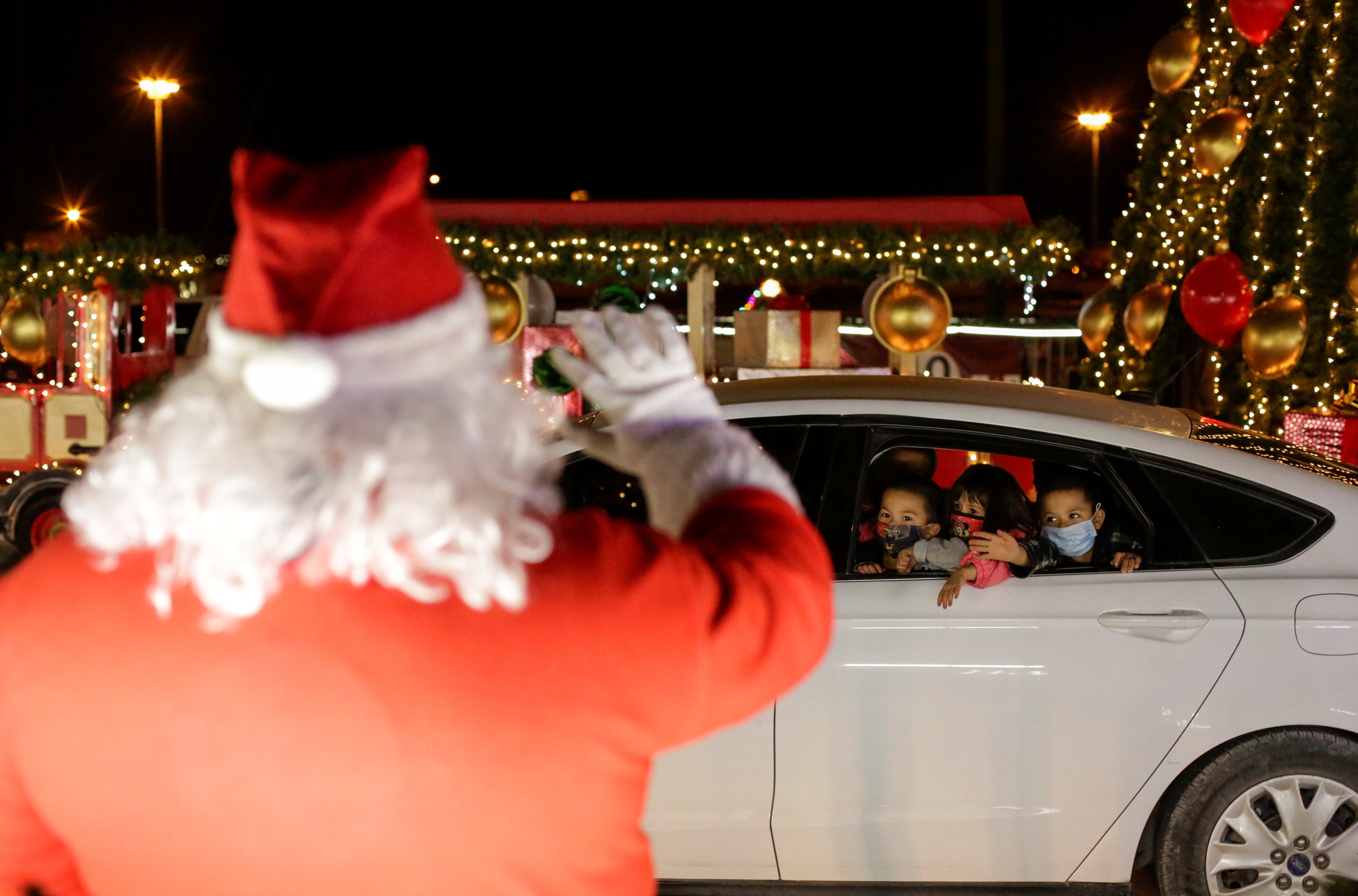 Children greet a person dressed as Santa Claus at a drive-thru Christmas village in Ciudad Juarez
