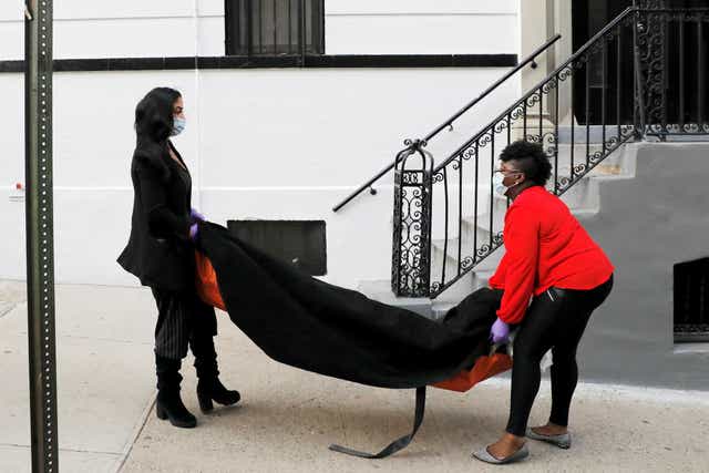 <p>Undertakers Alisha Narvaez and Nicole Warring carry the body of a dead person to the basement of the funeral home where they both work, in Harlem, New York City, in April</p>