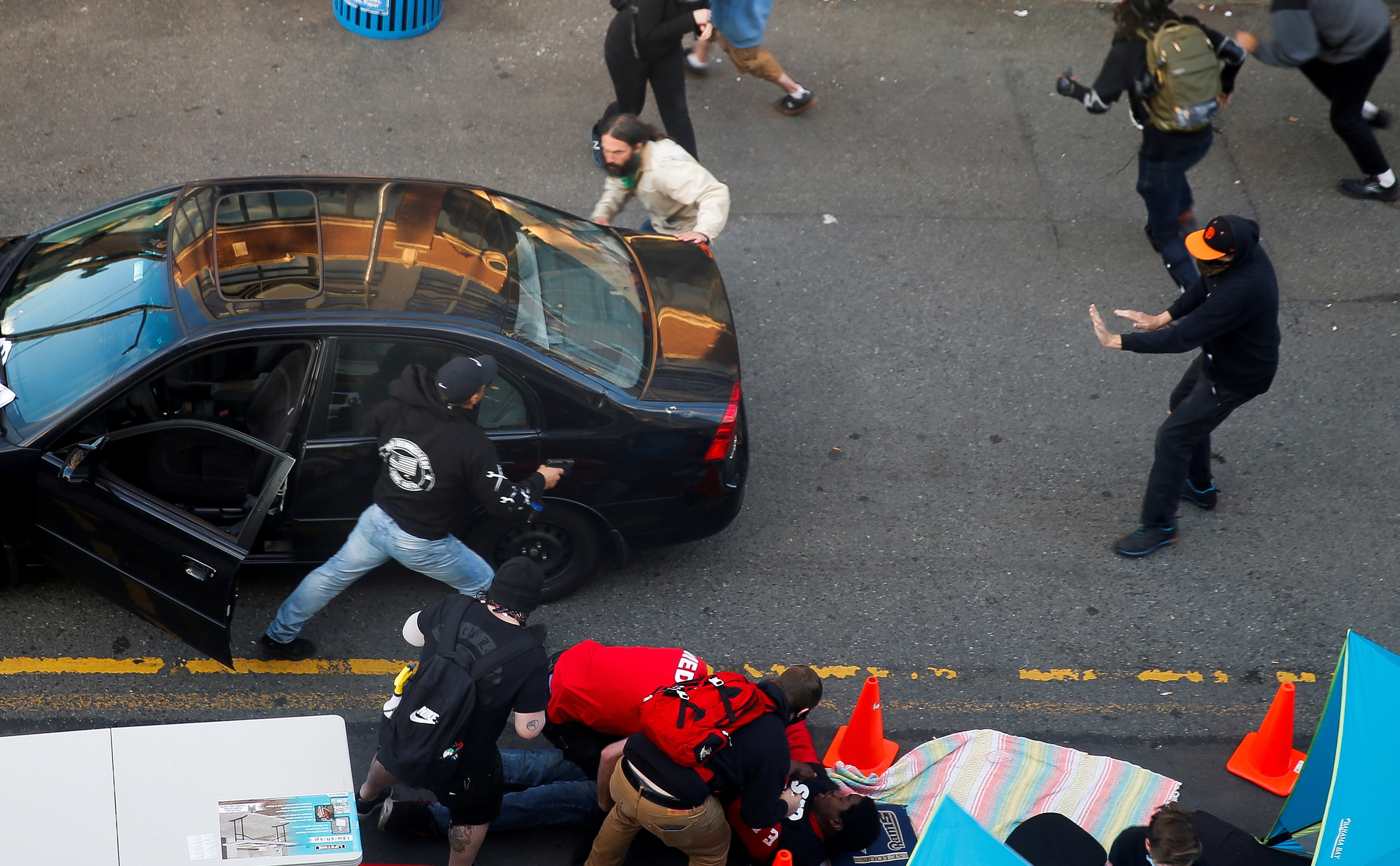 A man carrying a gun exits a vehicle as Daniel Gregory is tended to by medics after being shot in the arm by a driver who tried to drive through a protest against racial inequality in Seattle, Washington, in June