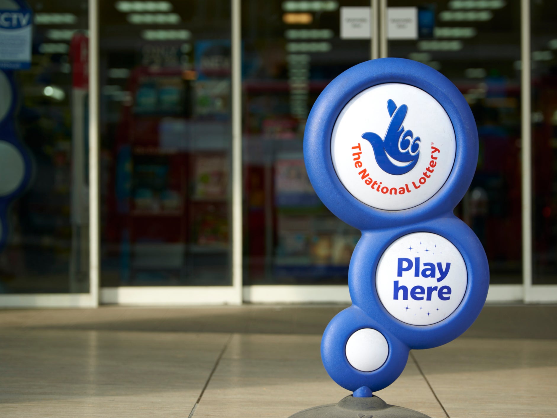 Blue National Lottery sign, showing its crossed fingers logo, in front of shop entrance