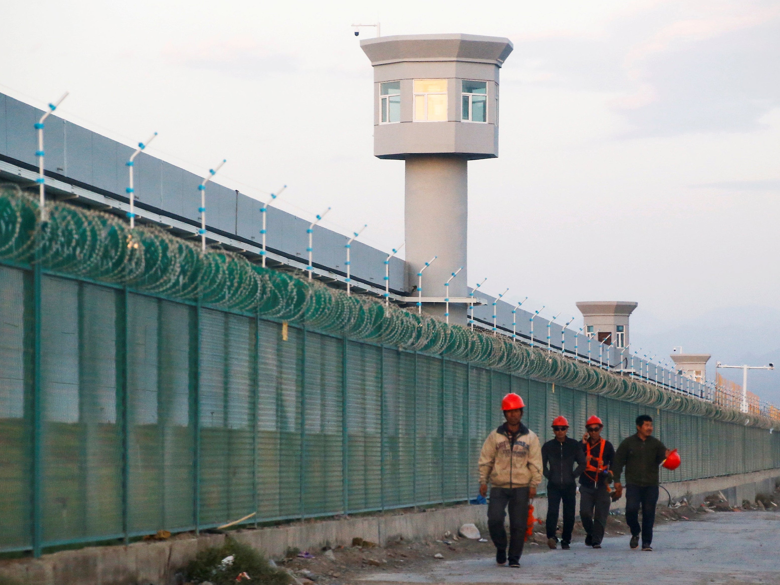 Workers walk by the perimeter fence of what is officially known as a vocational skills education centre in Dabancheng in Xinjiang