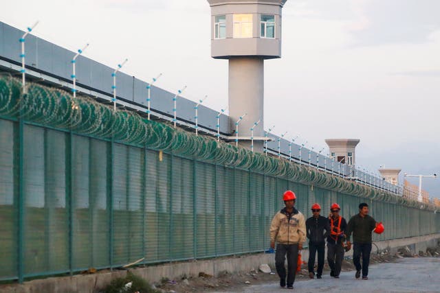 Workers walk by the perimeter fence of what is officially known as a vocational skills education centre in Dabancheng in Xinjiang