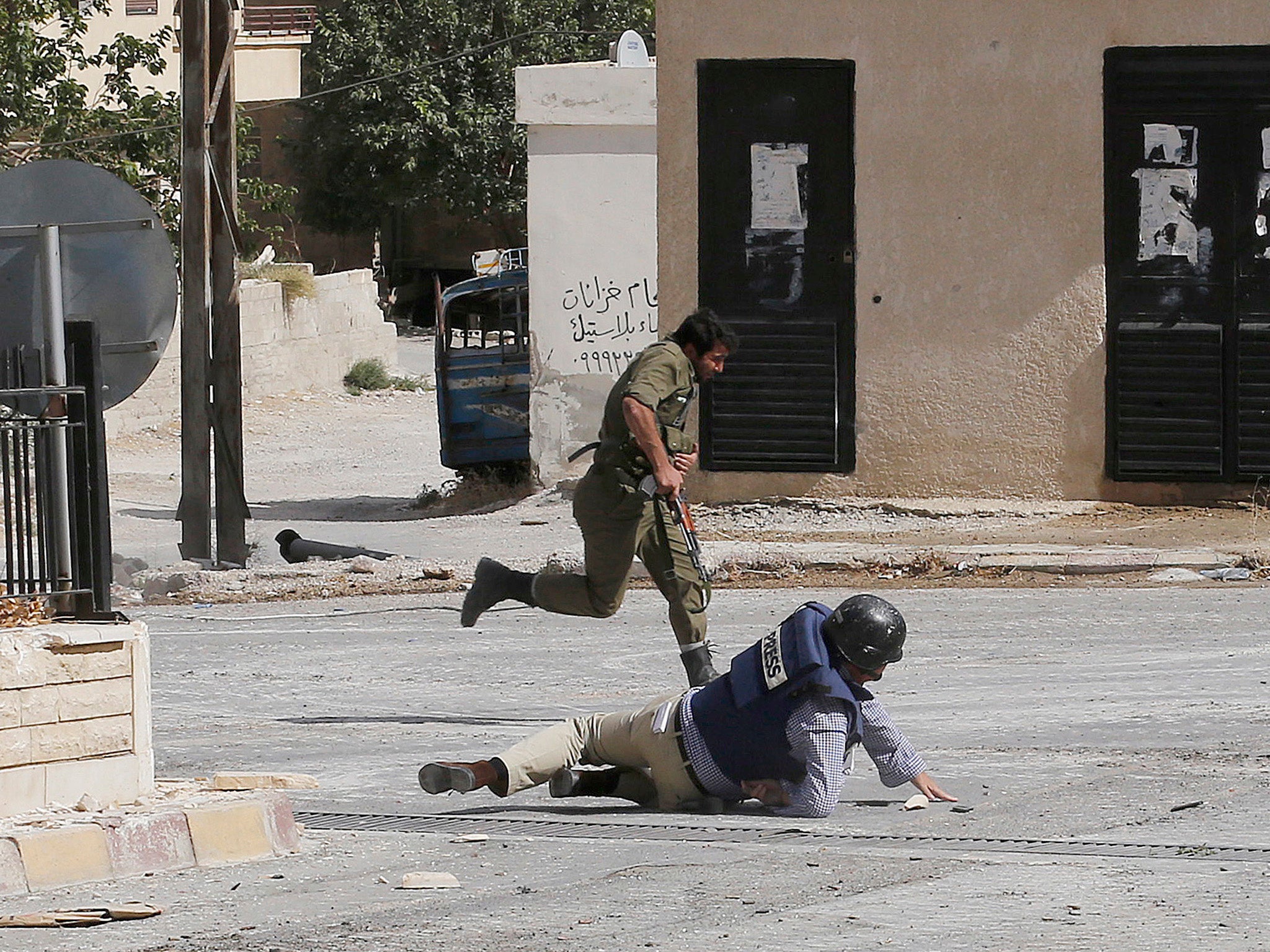 Reporter Sammy Ketz hits the ground as a Syrian soldier runs past during sniper fire in the ancient Christian Syrian town of Maalula