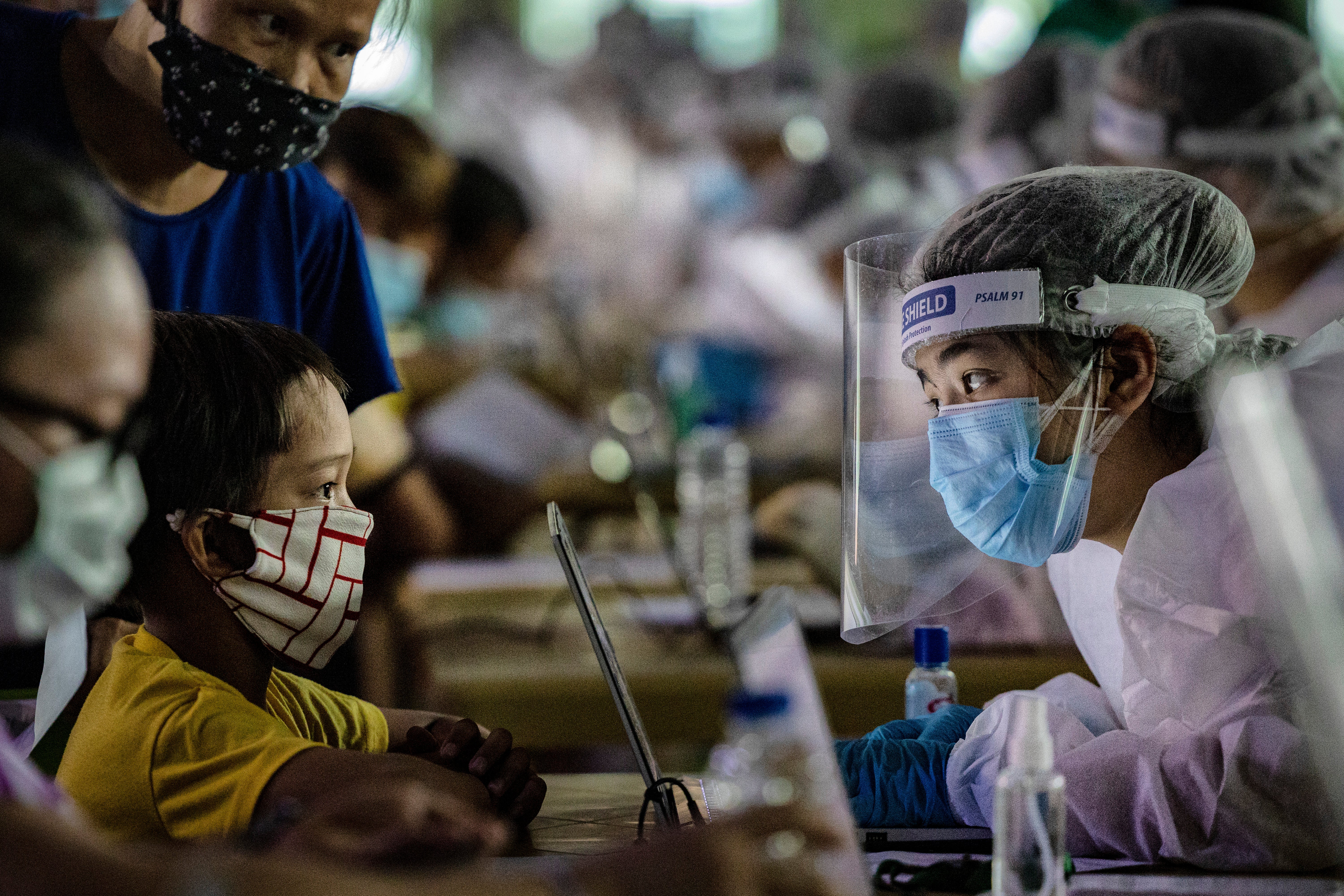 A medical worker wearing personal protective equipment interviews a child queueing for free COVID-19 swab testing at a basketball court on 6 August, 2020 in Navotas city, Metro Manila, Philippines. Residents in the country will now be made to wear full face shields, as well as face masks when out in public