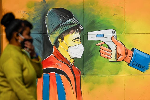 A woman wearing a facemask as a preventive measure against the Covid-19 coronavirus walks past a mural in New Delhi 