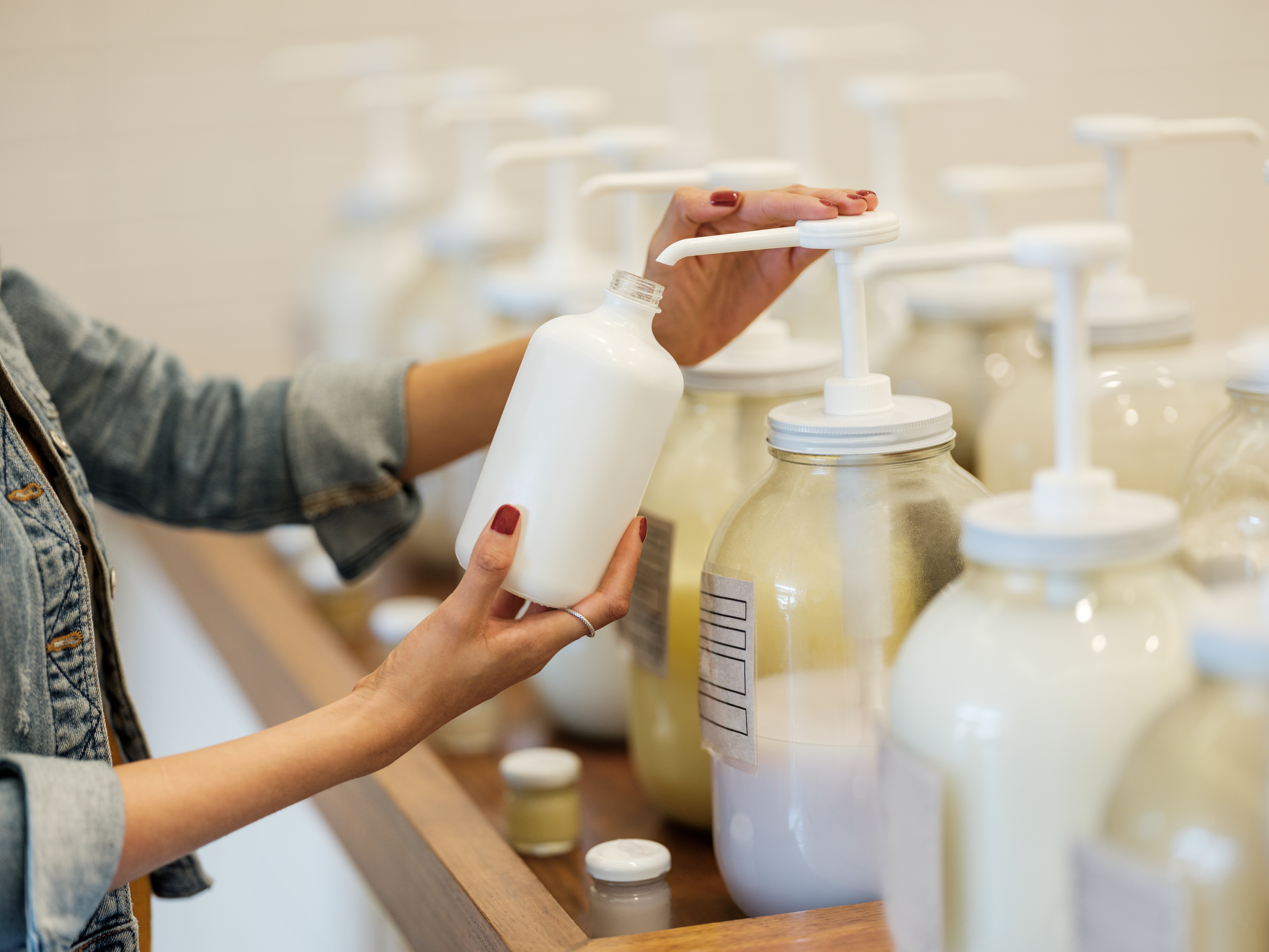 A woman holding and filling up glass container with lotion at the zero waste store.&nbsp;