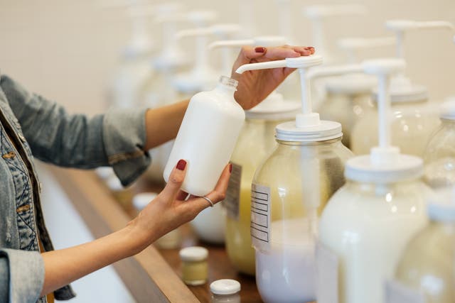 <p>A woman holding and filling up glass container with lotion at the zero waste store.&nbsp;</p>