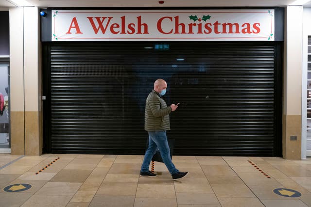 A man wearing a face mask walks past a closed Welsh Christmas store in Cardiff. All non-essential shops will close as of midnight, and people have been advised to stay home in a bid to curb the infection rates in one of the worst hit areas of the UK