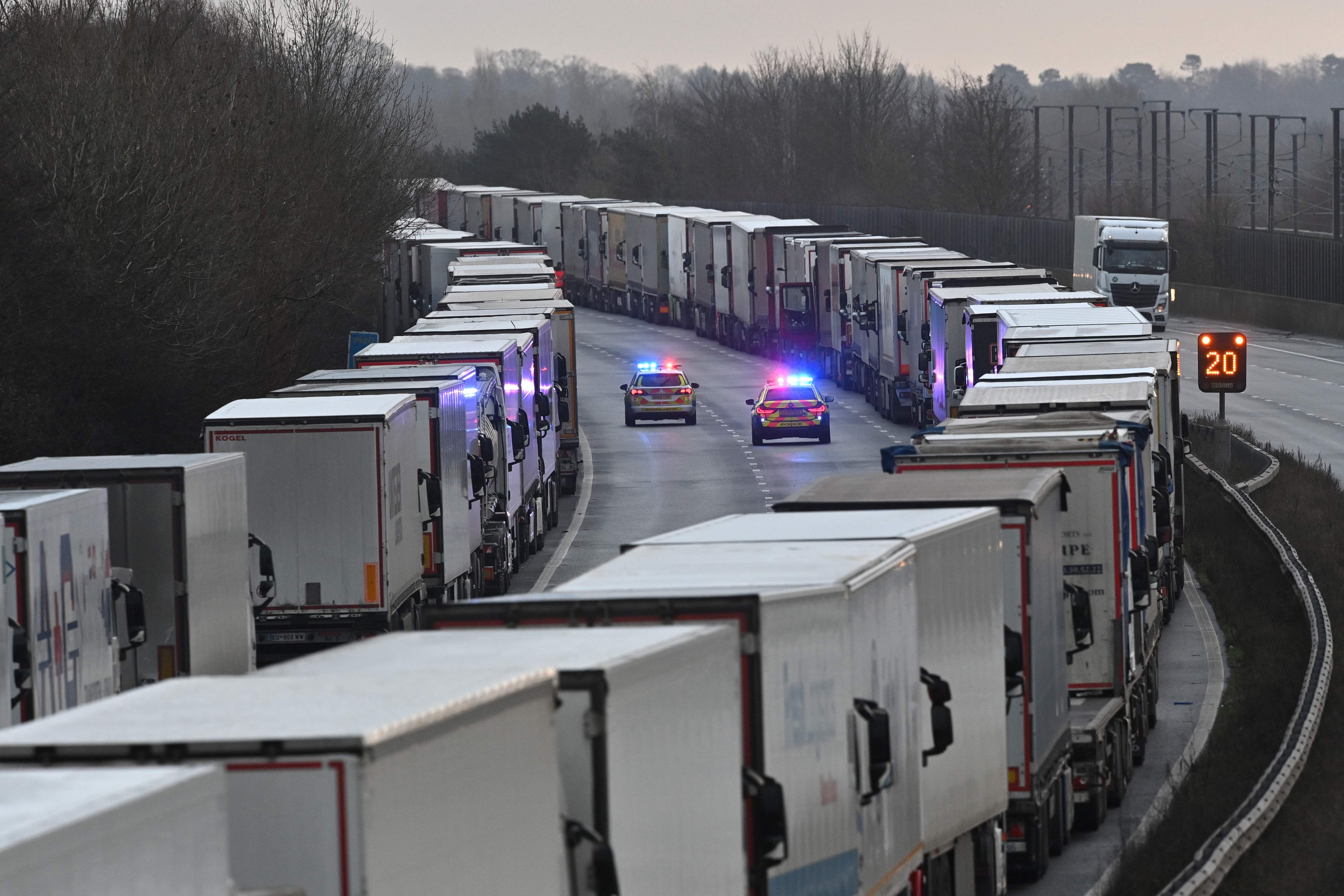 Police cars patrol as freight lorries and goods vehicles queue on a closed section of the M20 that leads to Dover