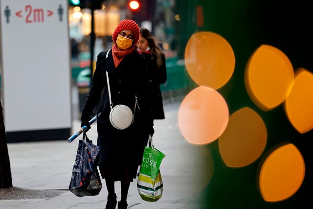 A pedestrian wearing a face mask or covering due to the COVID-19 pandemic, carries shopping bags and Christmas wrapping paper as they walk along Oxford Street in central London on 22 December, 2020.