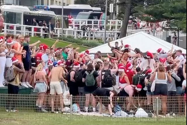 <p>Partygoers wearing Santa hats gather at Bronte Beach on Christmas Day</p>