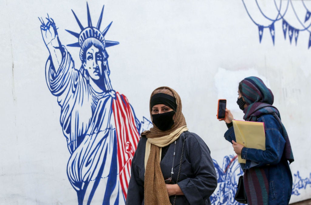 <p>Iranian women walk past a mural painted on the outer walls of the former US embassy in the capital Tehran</p>