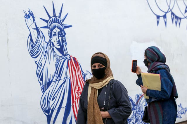 <p>Iranian women walk past a mural painted on the outer walls of the former US embassy in the capital Tehran</p>