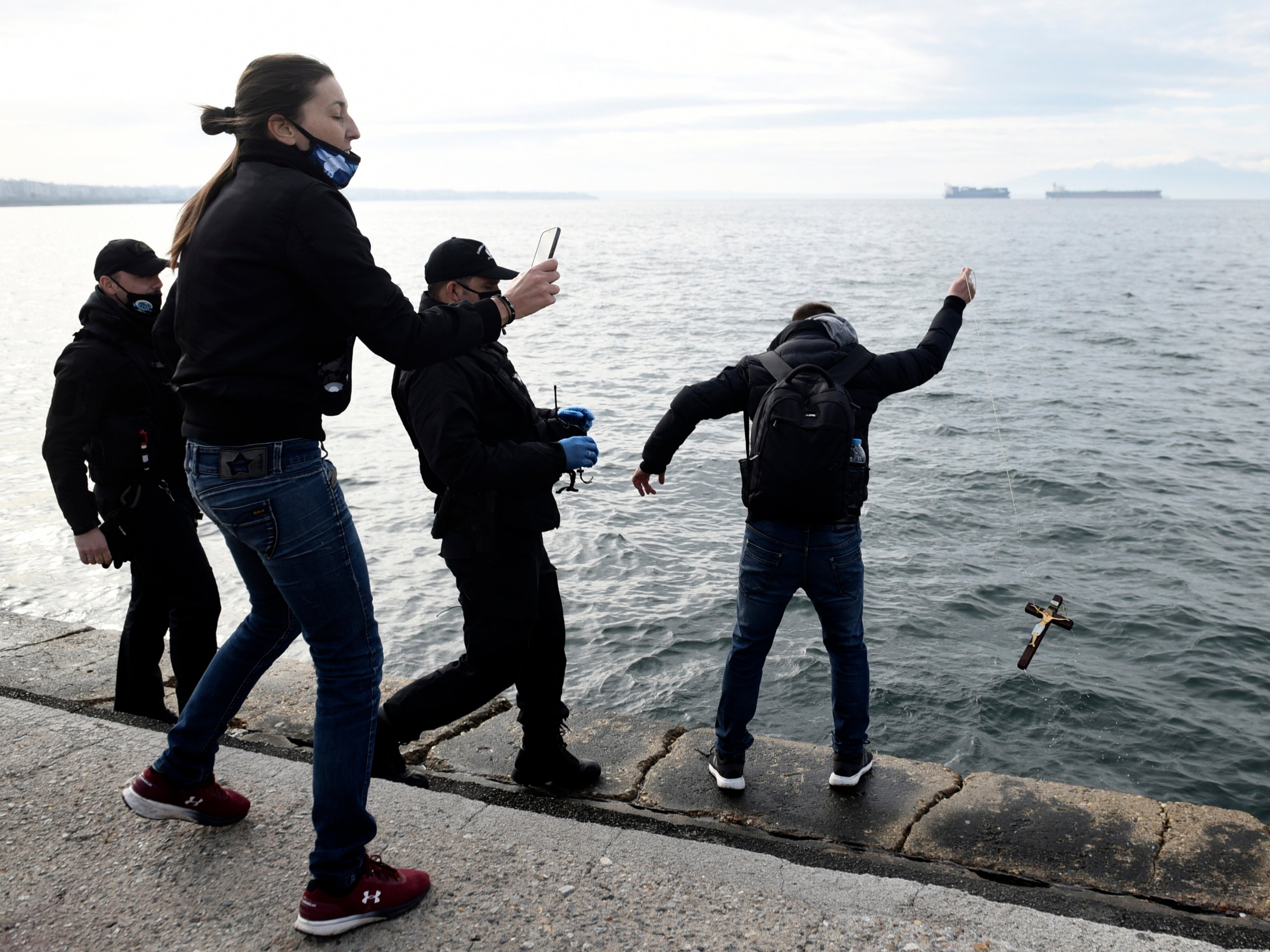 A man throws a cross into the sea as policemen go to detain him during Epiphany in the northern city of Thessaloniki
