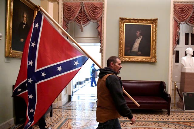 <p>A rioter carries a Confederate battle flag on the second floor of the Capitol near the entrance to the Senate after breaching security defences, in Washington, on 6 January 2021.</p>