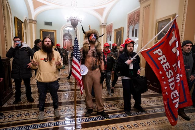 Jake Angeli, center, stands in the US Capitol dressed in fur and horns after Trump supporters stormed the building on 6 January in an effort to force legislators to overturn the election results.  