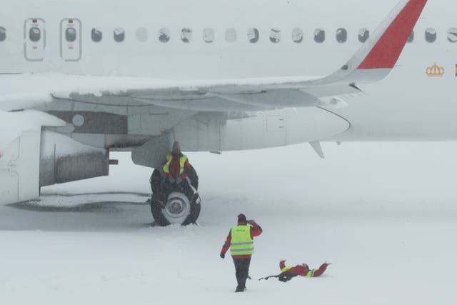 <p>An airport worker sits on the wheel of a parked snow-covered plane as one of his colleague takes a picture of another coworker lying on the snow at Adolfo Suarez Barajas airport, which is suspending flights due to heavy snowfall in Madrid</p>