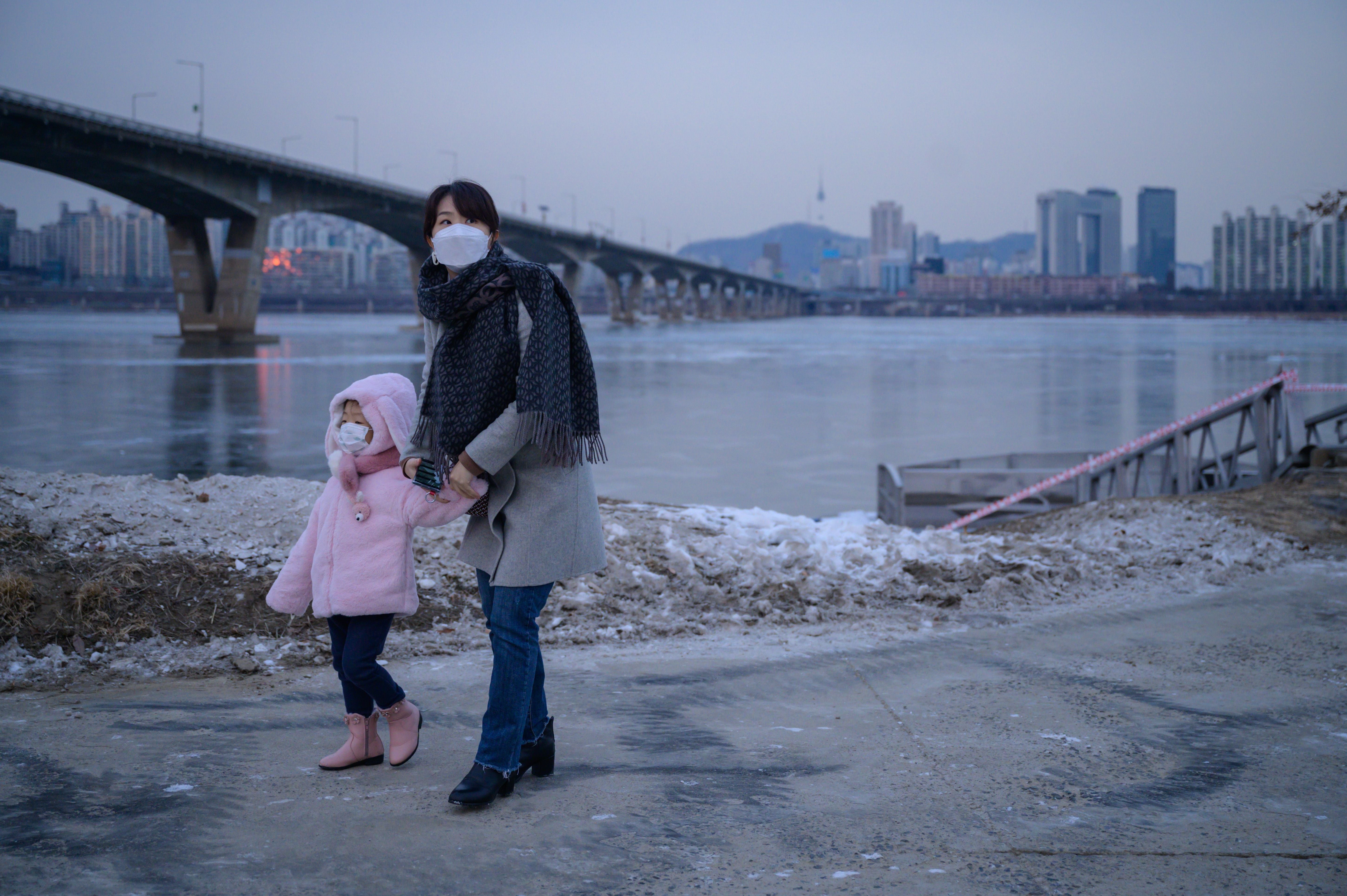 A photo taken on 10 January 2021 shows a woman and child standing before the frozen Han river and Seoul city skyline.
