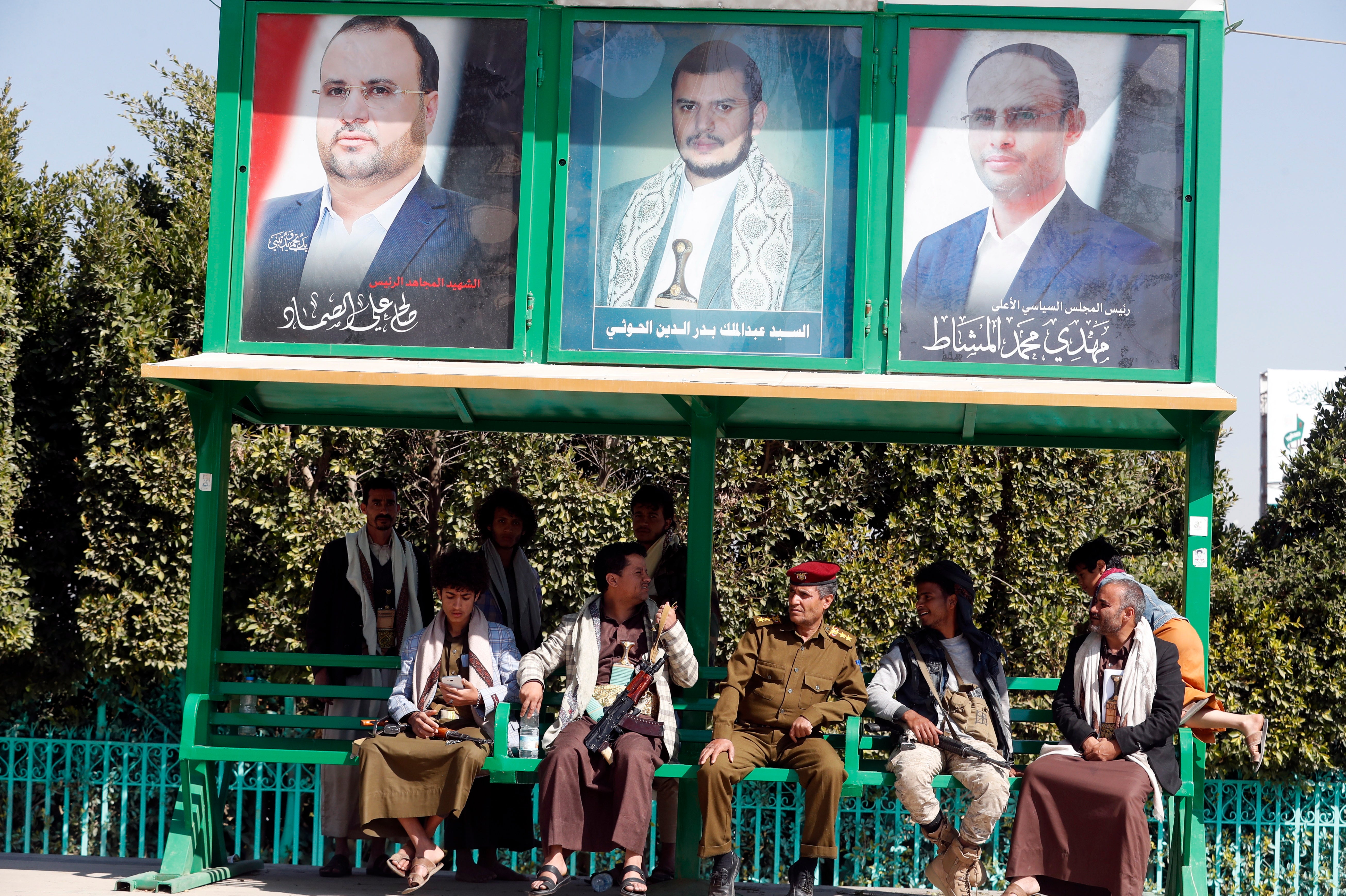 Armed militiamen and supporters of the Houthi movement sit under portraits of top Houthi leaders