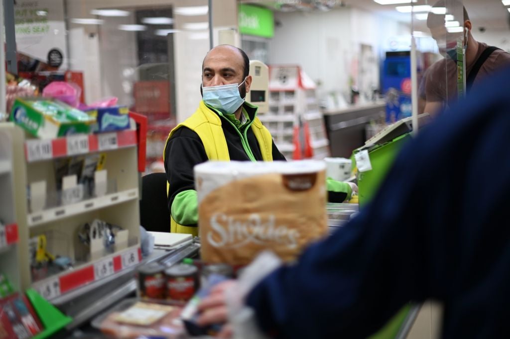 A shop worker wearing a protective face covering to combat the spread of the coronavirus serves customers at an Asda supermarket in London in December&nbsp;