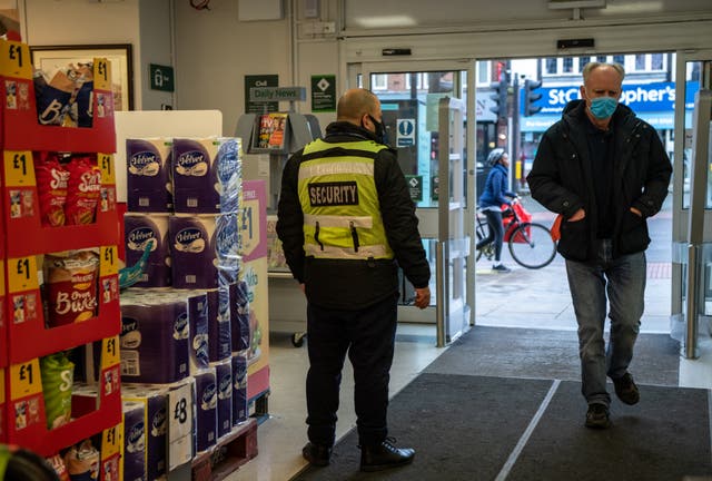  A security guard stands by the entrance to a Morrisons supermarket as a customer wearing a face mask enters the store