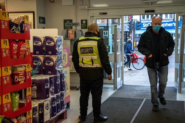  A security guard stands by the entrance to a Morrisons supermarket as a customer wearing a face mask enters the store