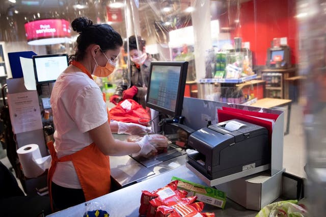 <p>A woman works on a checkout behind a plastic screen to reduce the risk of coronavirus transmission</p>