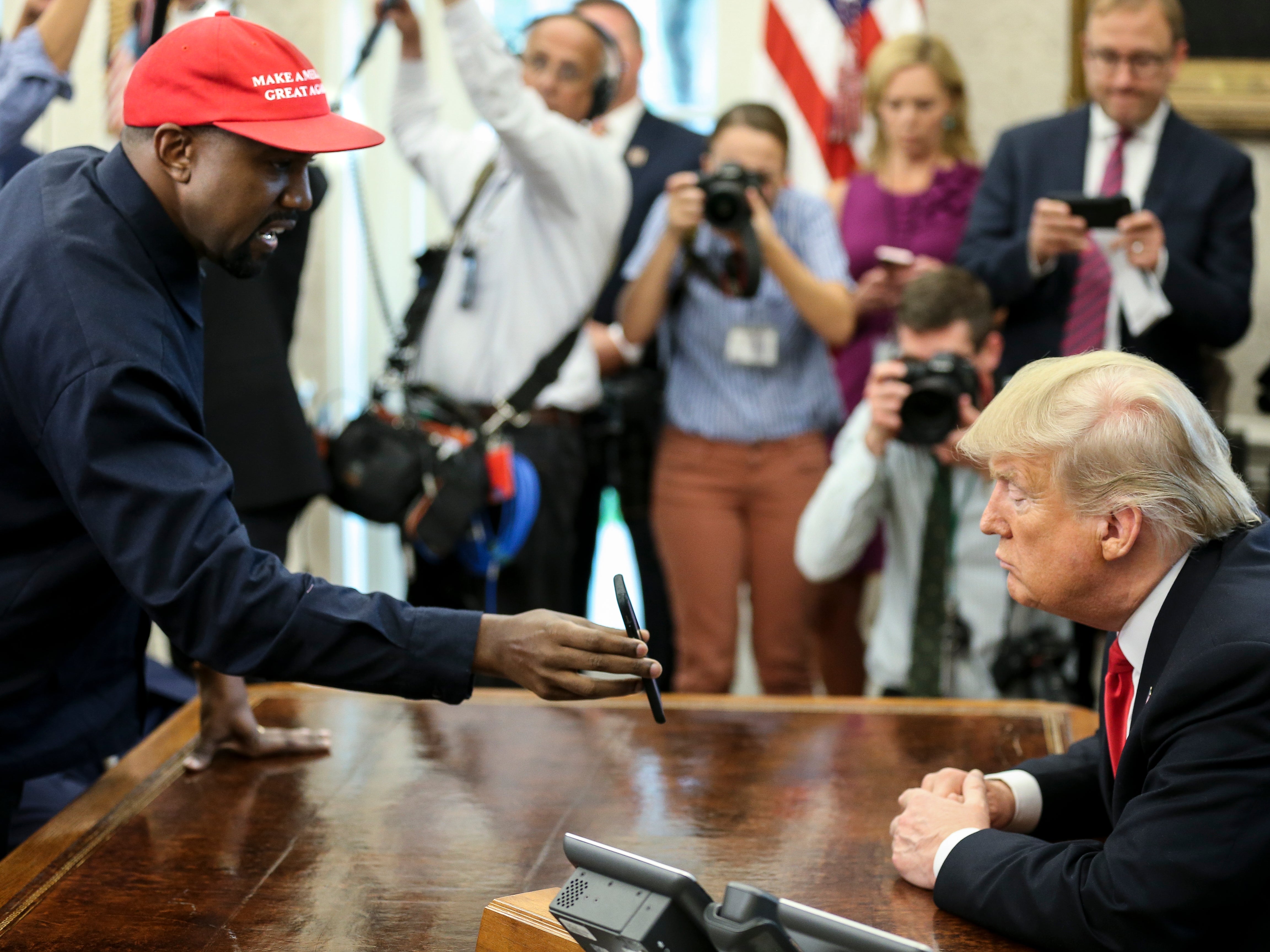 Kanye West shows a picture on a phone to Donald Trump during a meeting in the Oval office