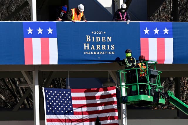 <p>Workers place Biden-Harris inauguration banners on the inaugural parade viewing stand across from the White House in Washington on 14 January 2021.</p>